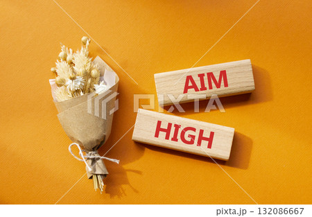 Aim High symbol. Wooden blocks with words Aim High. Beautiful orange background with bouquet of flowers. Business and Aim High concept. Copy space. Aim High symbol. Wooden blocks with words Aim High. Beautiful orange background with bouquet of flowers. Business and Aim High concept. Copy space. 132086667