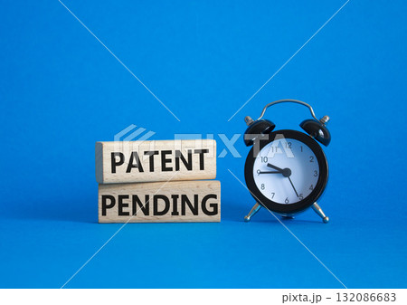 Patent Pending symbol. Wooden blocks with words Patent Pending. Beautiful blue background with alarm clock. Business and Patent Pending concept. Copy space. Patent Pending symbol. Wooden blocks with words Patent Pending. Beautiful blue background with alarm clock. Business and Patent Pending concept. Copy space. 132086683