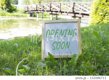 Opening soon symbol. Concept word Opening soon on white chalk blackboard. Beautiful meadow background with bridge. Business and Opening soon concept. Copy space. Opening soon symbol. Concept word Opening soon on white chalk blackboard. Beautiful meadow background with bridge. Business and Opening soon concept. Copy space. 132086711