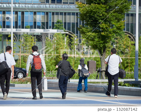 夏の朝の金沢駅西広場を渡る通勤中の会社員の姿	 夏の朝の金沢駅西広場を渡る通勤中の会社員の姿	 132087142