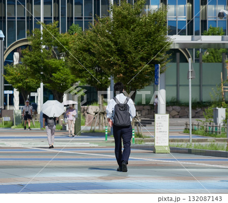 夏の朝の金沢駅西広場を渡る通勤中の会社員の姿	 夏の朝の金沢駅西広場を渡る通勤中の会社員の姿	 132087143