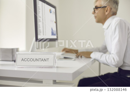 Name plate that reads Accountant with a man working on a computer in the background Name plate that reads Accountant with a man working on a computer in the background 132088146