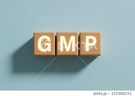 Wooden blocks with glowing letters spelling "GMP" create striking visual against blue pastel background, emphasizing pharmaceutical compliance in clean, minimal composition 132088251