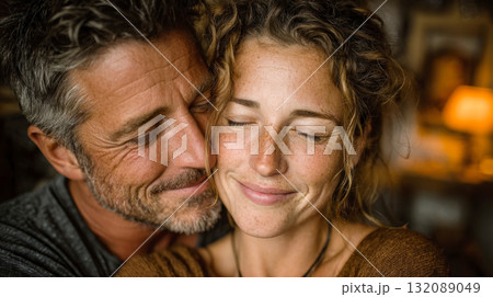 An intimate, heartfelt close-up portrait of a couple embracing. Both have their eyes closed and are smiling, conveying tender emotion, love, trust, and happiness in a lasting relationship 132089049
