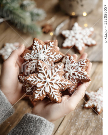 Hands holding homemade gingerbread snowflake cookies with white icing against a rustic wooden background. Perfect for Christmas baking, holiday treats, winter food, cozy mood, and festive themes Hands holding homemade gingerbread snowflake cookies with white icing against a rustic wooden background. Perfect for Christmas baking, holiday treats, winter food, cozy mood, and festive themes 132089057