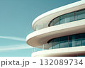 Modern architectural design featuring a curved building facade with large glass windows, showcasing sleek lines and a contemporary aesthetic against a clear blue sky 132089734