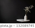 Minimalist arrangement featuring a white vase with delicate flowers on a round marble table against a dark background, creating a serene and elegant atmosphere for home decor, with copy space 132089745