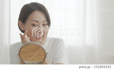 室内で鏡をみながら肌の調子を確認するミドル女性 室内で鏡をみながら肌の調子を確認するミドル女性 132091935