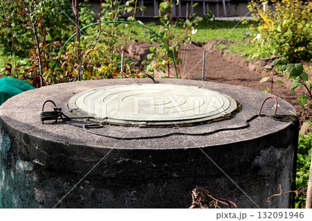A stone well with a closed lid against a garden backdrop on a sunny autumn day A stone well with a closed lid against a garden backdrop on a sunny autumn day 132091946