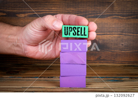 Hand holding green block with text UPSELL above stack of purple wooden blocks. Business growth Hand holding green block with text UPSELL above stack of purple wooden blocks. Business growth 132092627