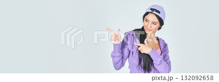 Young asian female in purple outfit and cap pointing sideways on light Young asian female in purple outfit and cap pointing sideways on light 132092658