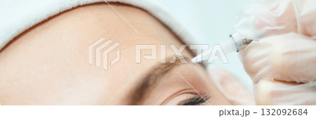 Close-up of female eyebrow microblading procedure with gloved hand applying 132092684