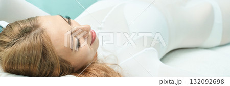 Relaxed young caucasian female in white outfit lying on bed with soft Relaxed young caucasian female in white outfit lying on bed with soft 132092698