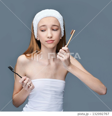Young caucasian female teen in skincare routine holding toothbrushes, choosing 132092767