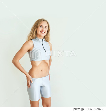 Smiling caucasian young adult female in activewear posing confidently against 132092822