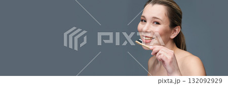 Smiling caucasian female adult holding bamboo toothbrush against gray Smiling caucasian female adult holding bamboo toothbrush against gray 132092929