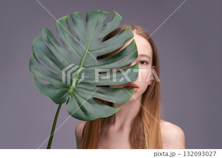 Caucasian female young model with monstera leaf covering face on grey background Caucasian female young model with monstera leaf covering face on grey background 132093027