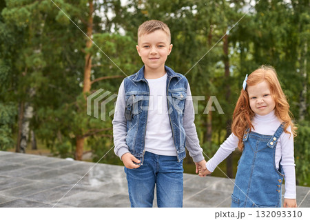 Young caucasian male child and female child holding hands outdoors in denim 132093310