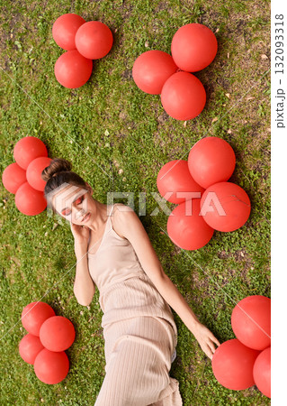 Young caucasian female lying on grass with red balloons in beige dress, eyes Young caucasian female lying on grass with red balloons in beige dress, eyes 132093318