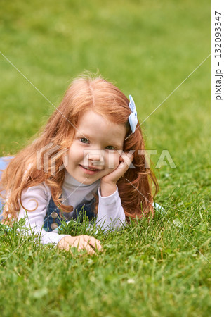Smiling caucasian young girl with red hair lying on grass outdoors enjoying 132093347