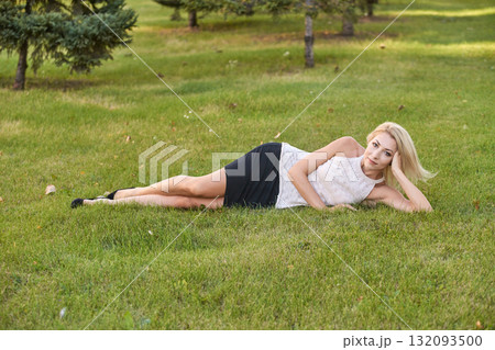 Caucasian young female lying on grass in park wearing white top and black skirt Caucasian young female lying on grass in park wearing white top and black skirt 132093500
