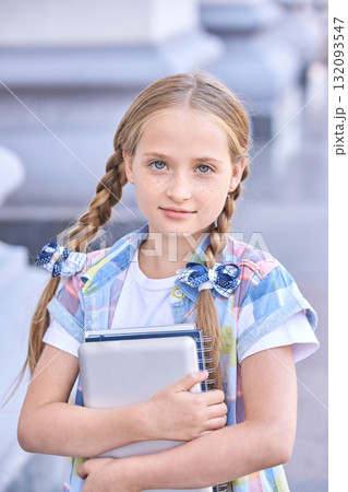 Caucasian female child with blonde braids holding laptop outdoors in casual Caucasian female child with blonde braids holding laptop outdoors in casual 132093547