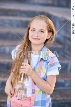 Smiling caucasian young girl holding bottle on stone steps outdoors in casual 132093576