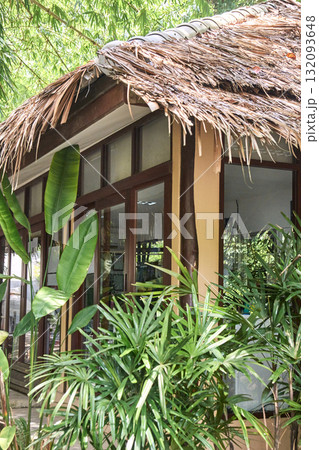Tropical hut with palm fronds and lush greenery in a serene garden setting Tropical hut with palm fronds and lush greenery in a serene garden setting 132093648
