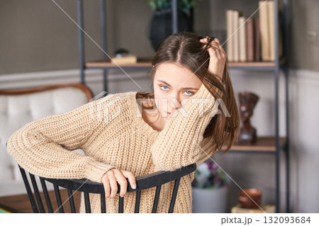 Young caucasian female resting on chair in cozy living room with bookshelf Young caucasian female resting on chair in cozy living room with bookshelf 132093684