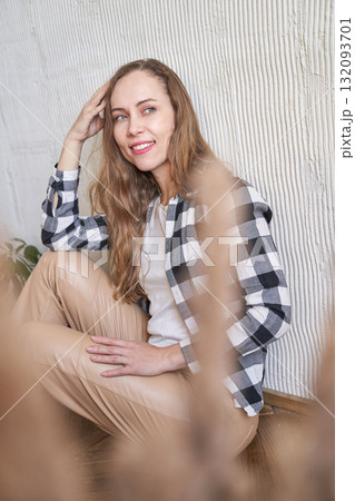Caucasian young adult female in checkered shirt sitting indoors with natural 132093701