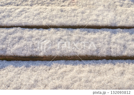 Close-up of snow-covered wooden planks creating a textured winter surface Close-up of snow-covered wooden planks creating a textured winter surface 132093812