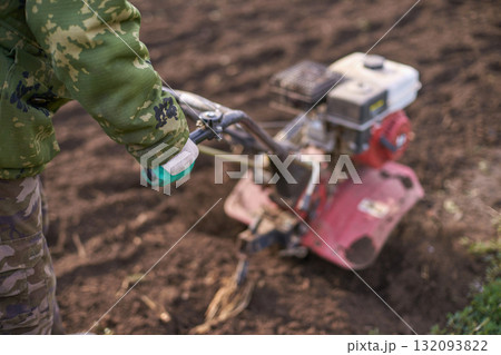 Adult male using tiller in field wearing camouflage clothing for farming 132093822