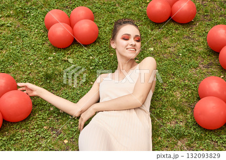 Young caucasian woman relaxing on grass with red balloons, enjoying outdoor 132093829