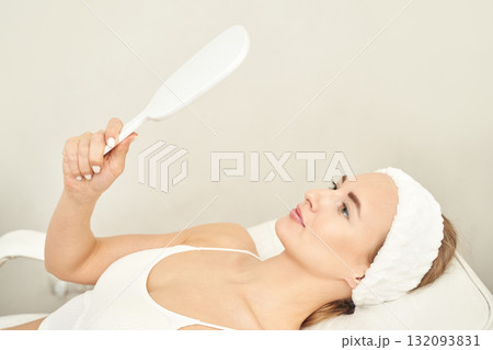 Young caucasian female relaxing in spa, holding hand mirror, wearing headband Young caucasian female relaxing in spa, holding hand mirror, wearing headband 132093831