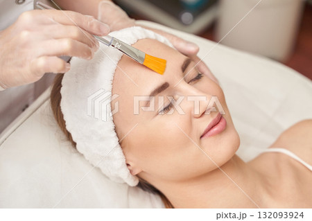 Young caucasian female receiving facial treatment with brush by professional 132093924