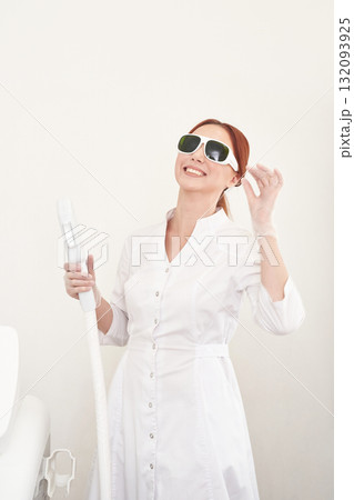 Smiling caucasian female adult in white coat with laser equipment in clinic 132093925