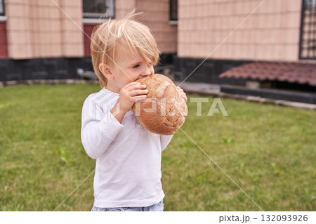 Blond caucasian child enjoying bread in outdoor urban yard setting Blond caucasian child enjoying bread in outdoor urban yard setting 132093926