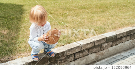 Blond caucasian child sitting outdoors holding large piece of bread in sunlit Blond caucasian child sitting outdoors holding large piece of bread in sunlit 132093964