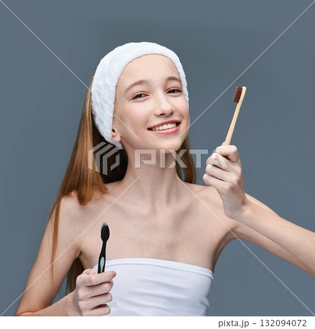 Smiling caucasian teen girl holding toothbrushes in bathroom attire Smiling caucasian teen girl holding toothbrushes in bathroom attire 132094072