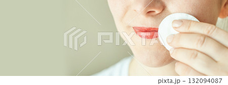 Caucasian female using cotton pad to remove lipstick from face close-up 132094087