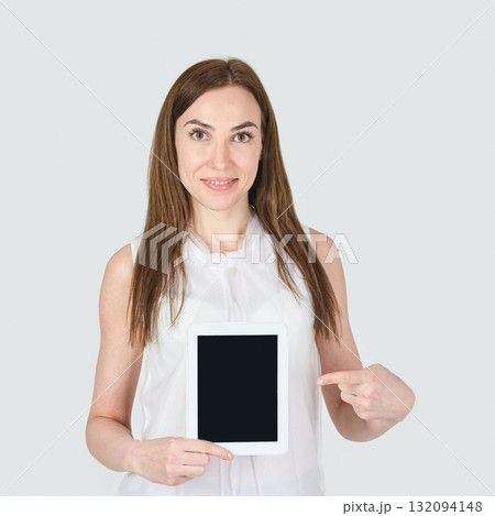 Young caucasian female pointing at tablet display in casual white attire 132094148