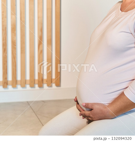 Pregnant caucasian female sitting indoors holding belly peaceful maternity 132094320