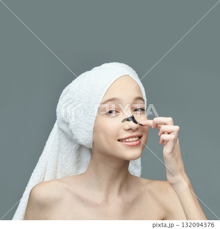 Young caucasian female applying face mask in skincare routine with towel Young caucasian female applying face mask in skincare routine with towel 132094376
