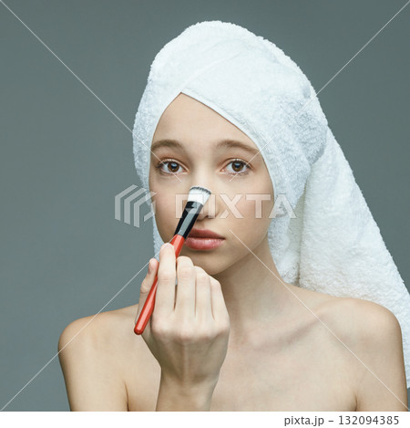 Young caucasian female applies makeup with brush in skincare routine Young caucasian female applies makeup with brush in skincare routine 132094385