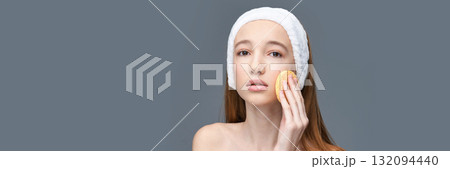 Young caucasian female using facial sponge for skincare on grey background 132094440