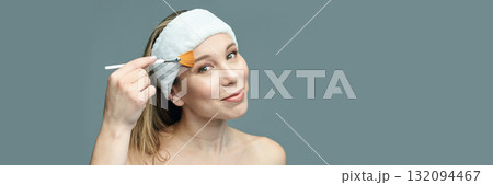 Caucasian female young adult applying facial mask with brush on gray background Caucasian female young adult applying facial mask with brush on gray background 132094467