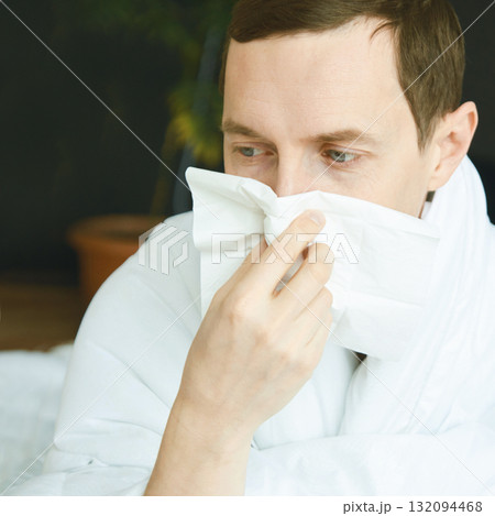 Young caucasian male with cold using tissue for runny nose in indoor setting Young caucasian male with cold using tissue for runny nose in indoor setting 132094468