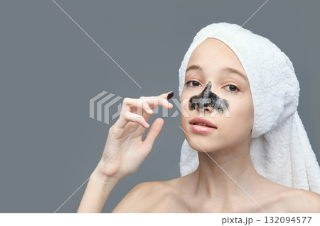 Young caucasian female applying charcoal face mask with towel on head 132094577