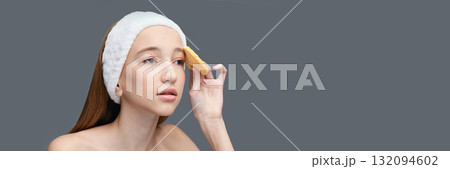 Young caucasian female adult using cosmetic sponge for skincare routine on grey Young caucasian female adult using cosmetic sponge for skincare routine on grey 132094602