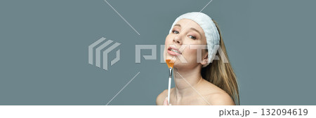 Young caucasian female applies makeup with brush against grey background Young caucasian female applies makeup with brush against grey background 132094619